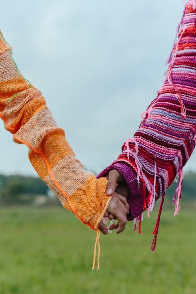 Two people wearing colorful sweaters holding hands in a serene outdoor setting.